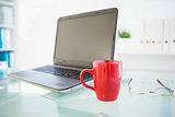 Laptop on desk with red mug and glasses