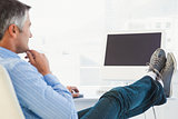 Relaxed man with feet on desk using computer