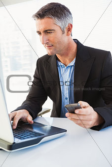 Businessman using laptop and holding smartphone
