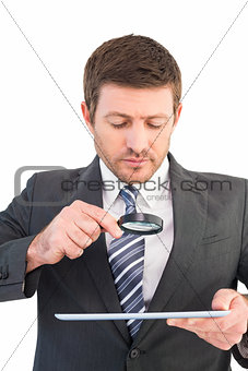 Businessman looking at tablet with magnifying glass