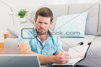 Focus man looking at is laptop and writing on a notebook