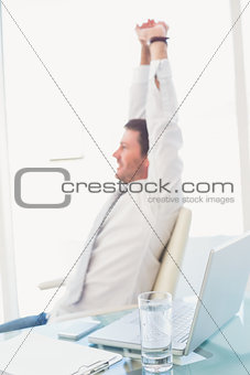 Smiling businessman stretching at desk