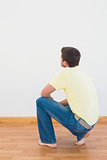 Casual man crouching on floor looking at wall at home