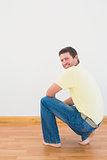 Casual man crouching on floor looking at wall at home