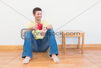 Casual man sitting on floor holding a mug at home