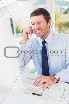 Smiling businessman phoning at his desk