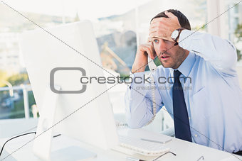 Shocked businessman on phone at his desk