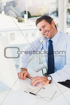 Smiling businessman working and phoning at his desk