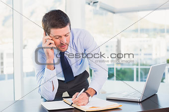 Businessman writing and phoning at his desk