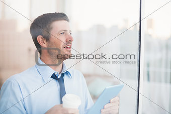 Businessman holding disposable cup and tablet looking out the window