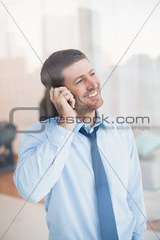 Smiling businessman looking out window on the phone