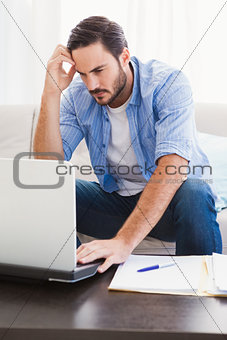 Worried man sitting at table using laptop to pay his bills