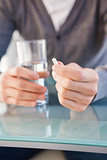 Mid section of a man holding glass of water and pill