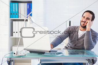 Businessman smiling at camera working on laptop