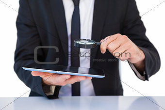 Businessman looking at his tablet through magnifying glass