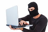 Focused burglar with balaclava holding laptop