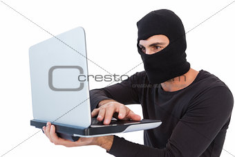 Focused burglar with balaclava holding laptop