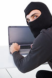 Burglar hacking into laptop while looking at camera