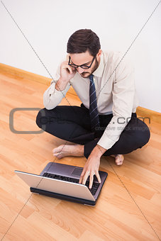 Businessman sitting on floor using mobile phone and laptop