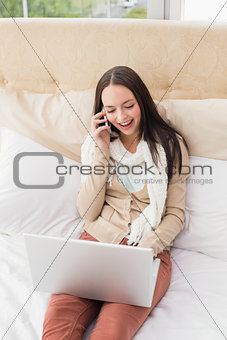 Pretty brunette using laptop on bed making phone call