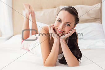 Pretty brunette smiling at camera on bed