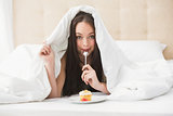 Pretty brunette eating cupcake in bed