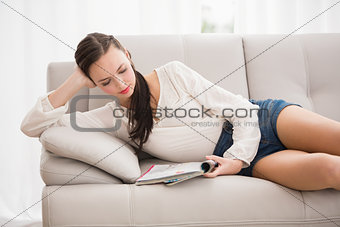 Pretty brunette reading magazine on the couch