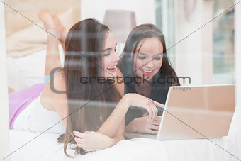 Pretty friends using laptop on bed