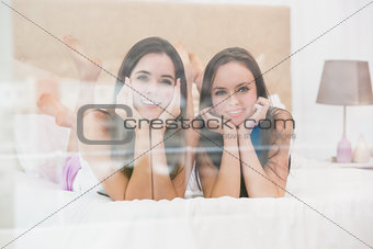 Pretty friends smiling at camera on bed