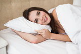 Pretty brunette lying in bed smiling at camera