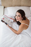 Pretty brunette reading magazine on bed
