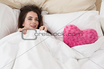 Pretty brunette in bed with heart cushion
