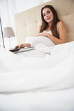 Pregnant brunette using laptop in bed