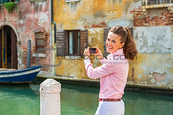 Happy young woman in venice, italy taking photo