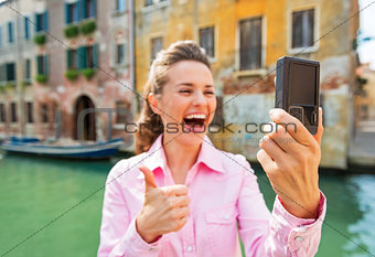 Closeup on happy young woman showing thumbs up and making selfie