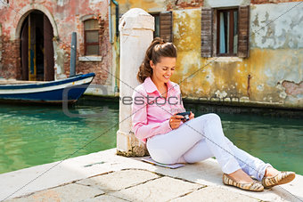 Smiling young woman sitting on street and checking photos in cam
