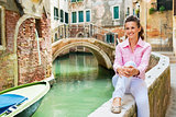Happy young woman sitting on bridge in venice, italy