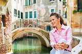 Happy young woman sitting on bridge in venice, italy and looking