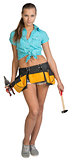Pretty girl in tool belt holding scissors for metal cutting and hammer. Full length