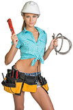 Pretty girl in helmet, shorts, shirt, tool belt with tools holding flexible hose and wrench