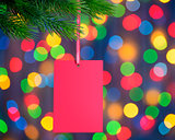 Christmas Greeting Card on the Fir Branch on the Holiday Lights Background