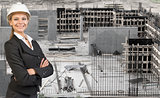 Beautiful businesswoman in helmet standing with crossed arms. Construction site as backdrop