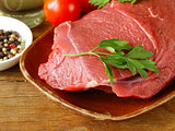 fresh raw beef meat with pepper and herbs on wooden plate