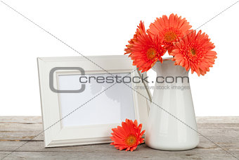 Orange gerbera flowers and photo frame on wooden table