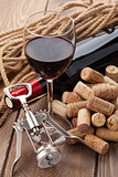 Glass of red wine, bottle, heap of corks and corkscrew