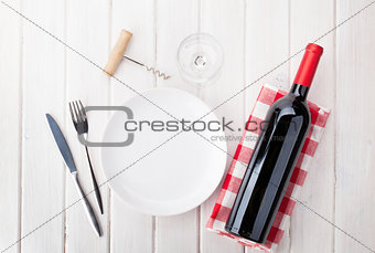 Table setting with empty plate, wine glass and red wine bottle