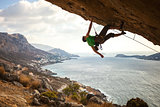 Male climber on overhanging rock against beautiful view of coast below