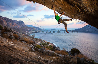 Male climber climbing overhanging rock against beautiful view of coast below