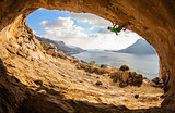 Young man lead climbing in cave with beautiful view in background