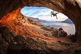 Female rock climber posing while climbing along roof in cave at sunset